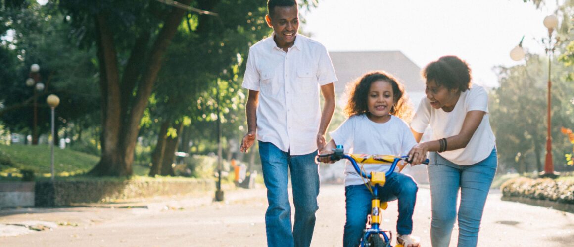A family walking with a child learning to ride a bike in a park
