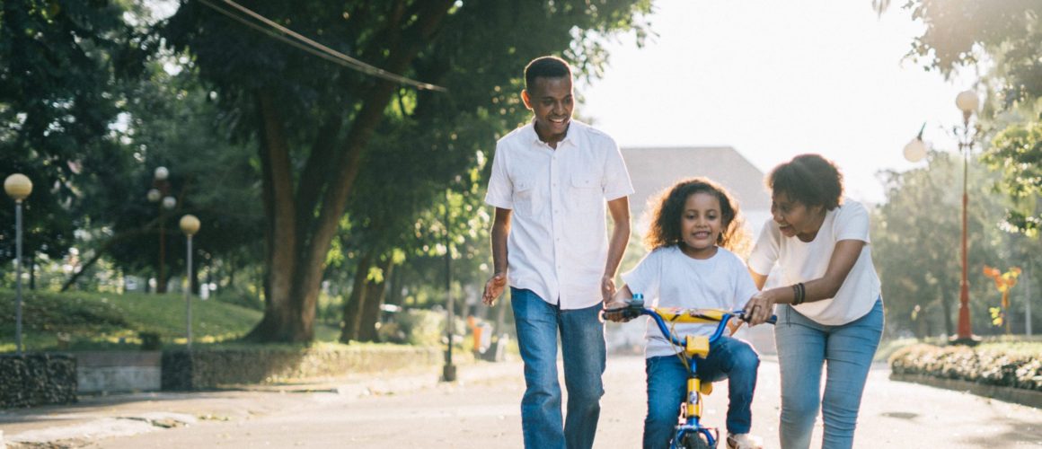 A family walking with a child learning to ride a bike in a park