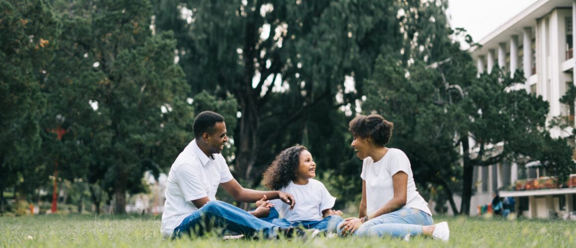A family of three enjoying time together on the grass in a park.