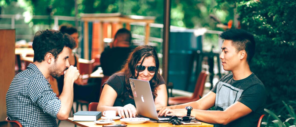 Three people working on laptops at an outdoor cafe.